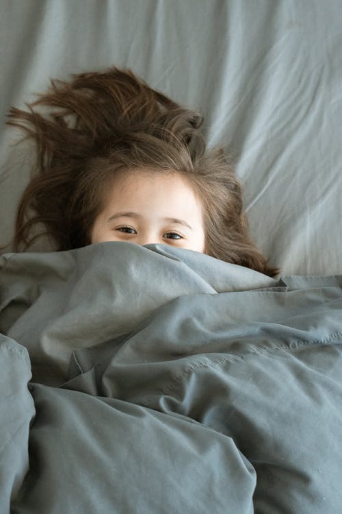 躺在床上的女孩覆盖着蓝色毯子 · 免费素材图片