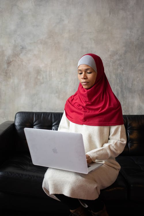 红色头巾的女人坐在黑色皮革沙发上 · 免费素材图片