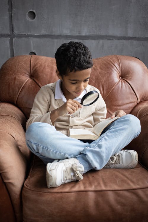 灰色毛衣和蓝色牛仔牛仔裤，坐在棕色沙发上的男孩 · 免费素材图片