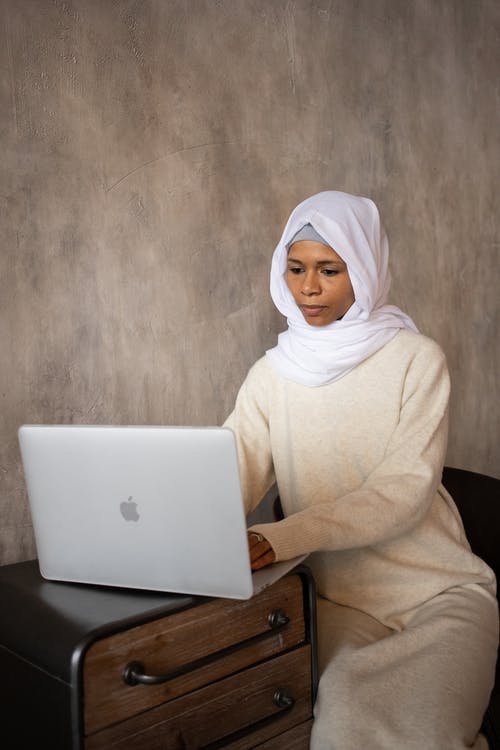 坐在沙发上使用macbook的白色头巾的女人 · 免费素材图片