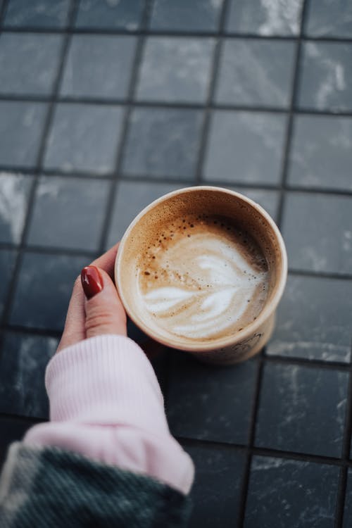 拿着带有棕色液体的白色陶瓷杯的人 · 免费素材图片