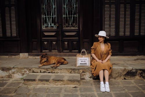 棕色外套坐在旁边的棕色短外套大狗的混凝土长凳上的女人 · 免费素材图片