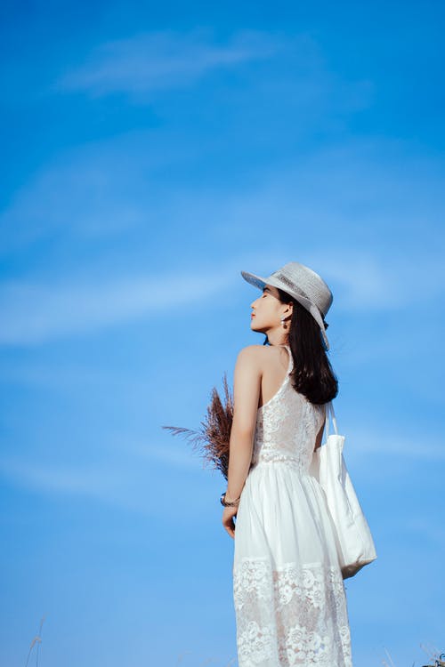 白色无袖连衣裙穿着白色太阳帽站在蓝蓝的天空下的女人 · 免费素材图片