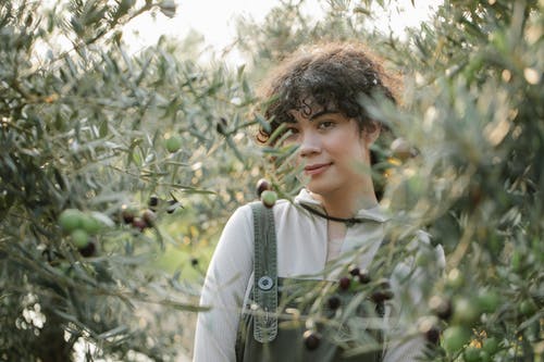 站在绿色的植物附近的白色羊毛衫的女人 · 免费素材图片