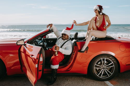 男人和女人在圣诞老人的衣服，坐在一辆红色的敞篷汽车 · 免费素材图片