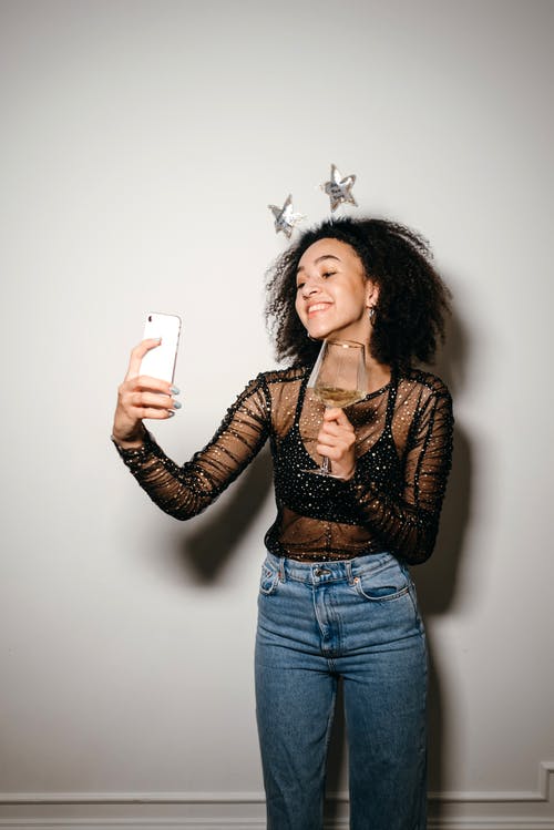 黑色的长袖衬衫和蓝色牛仔牛仔裤，拿着白色的智能手机的女人 · 免费素材图片