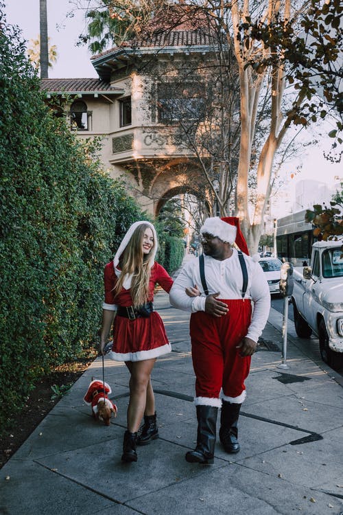 男人和女人在圣诞老人的衣服，在与狗的人行道上行走 · 免费素材图片