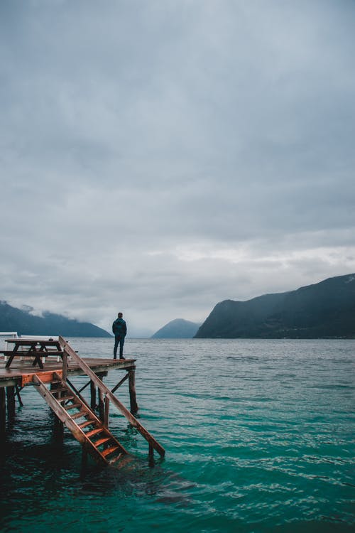 站在棕色木制码头上的黑夹克的男人 · 免费素材图片