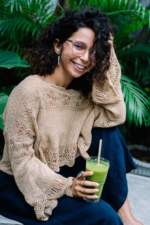 女人穿着米色针织毛衣，拿着绿色的杯子 · 免费素材图片