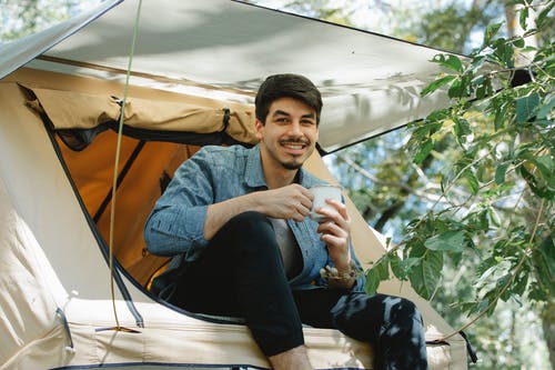 灰色长袖衬衫和蓝色牛仔牛仔裤，坐在白色帐篷上的男人 · 免费素材图片