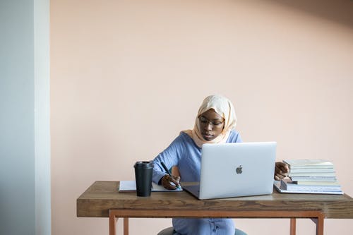 白头巾的女人在棕色的木桌上使用macbook空气 · 免费素材图片