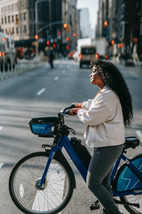 白色长袖衬衫和蓝色牛仔牛仔裤骑在蓝色自行车上的女人 · 免费素材图片