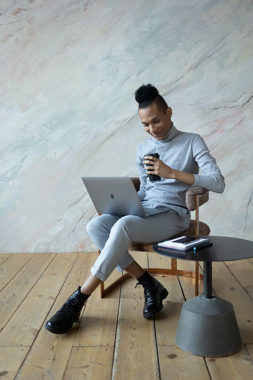 白色的长袖衬衫和灰色的裤子，坐在椅子上，使用macbook的男人 · 免费素材图片