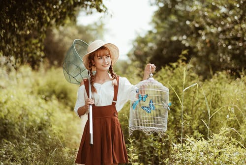 白色和红色的裙子，戴着棕色编织帽子站在绿草地上的女人 · 免费素材图片
