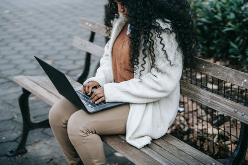 白色外套坐在棕色的木凳上，使用macbook的女人 · 免费素材图片