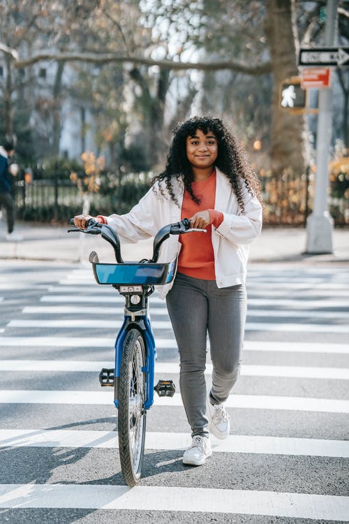 白色长袖衬衫和灰色的裤子，在行人专用车道上骑蓝色自行车的女人 · 免费素材图片