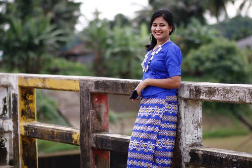 蓝船员的脖子t恤和蓝色和黄色的裙子，站在棕色木的女人 · 免费素材图片