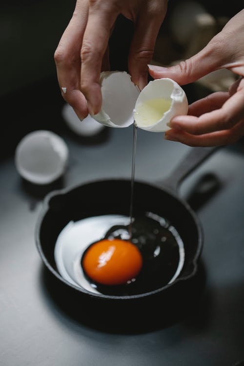 拿着鸡蛋在黑色煎锅上的人 · 免费素材图片