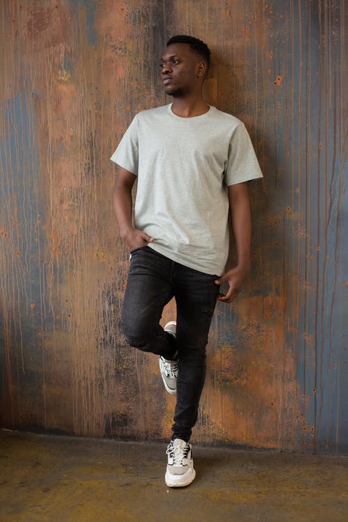 站在棕色木墙旁边的白色圆领t恤和黑色牛仔牛仔裤的男人 · 免费素材图片