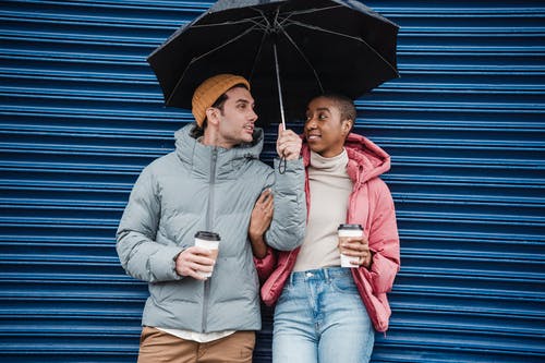 男人和女人坐在蓝色的木墙上拿着雨伞 · 免费素材图片