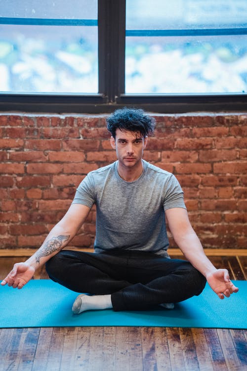 穿着灰色圆领t恤和黑色的裤子，坐在蓝色瑜伽垫上的男人 · 免费素材图片
