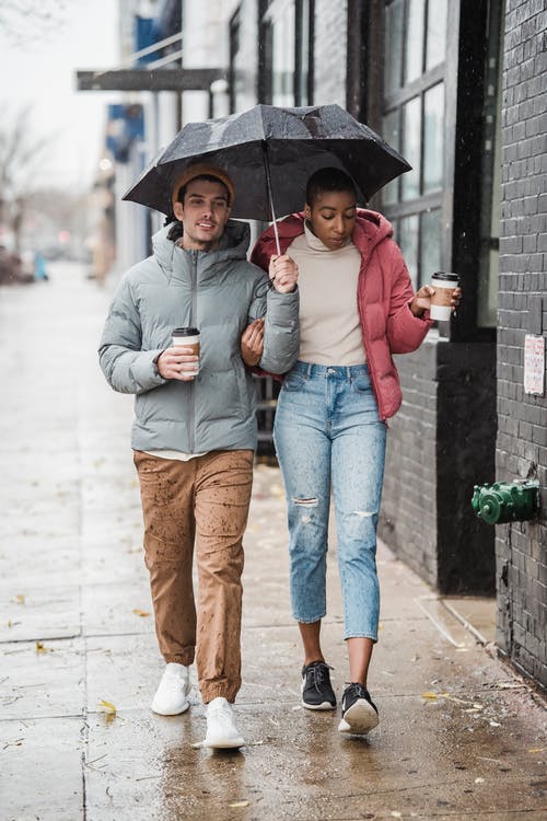 灰色连帽衫和蓝色牛仔牛仔裤的男人拿着伞在灰色连帽衫的女人旁边 · 免费素材图片