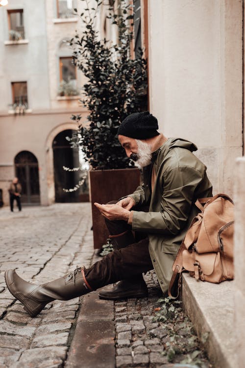 棕色夹克和黑色针织帽坐在人行道上的男人 · 免费素材图片