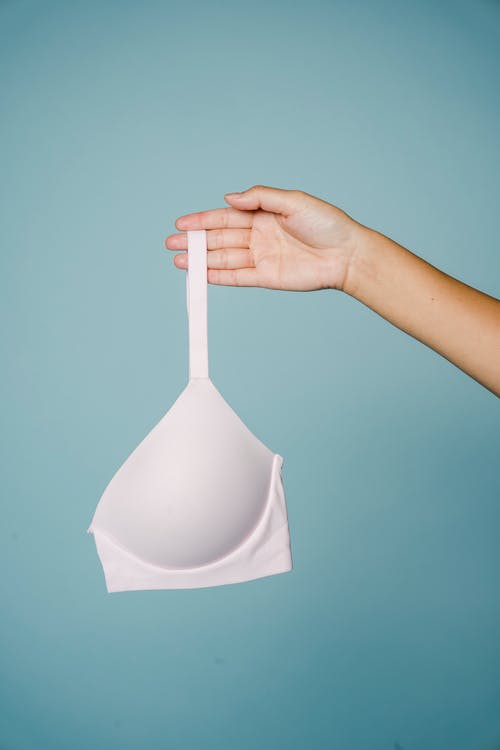 蓝墙上拿着白色胸罩的人 · 免费素材图片
