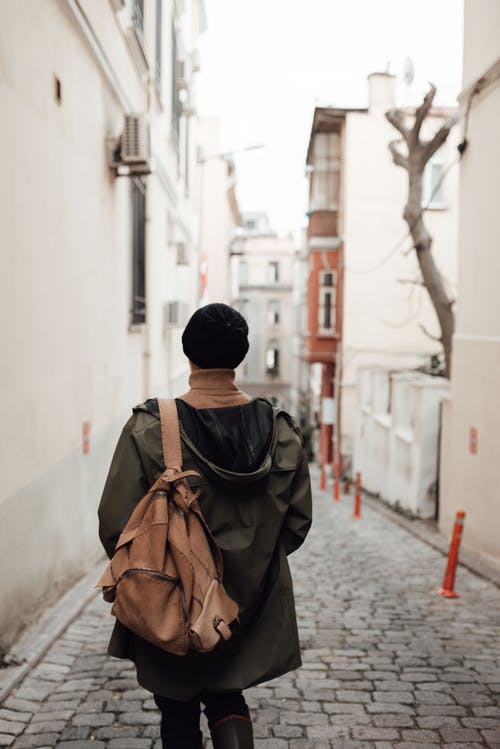 黑色针织帽和棕色背包走在大街上的人 · 免费素材图片
