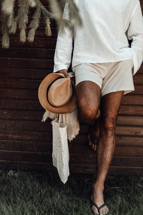 站在棕色木墙旁边的白色长袖衬衫和棕色软呢帽的男人 · 免费素材图片