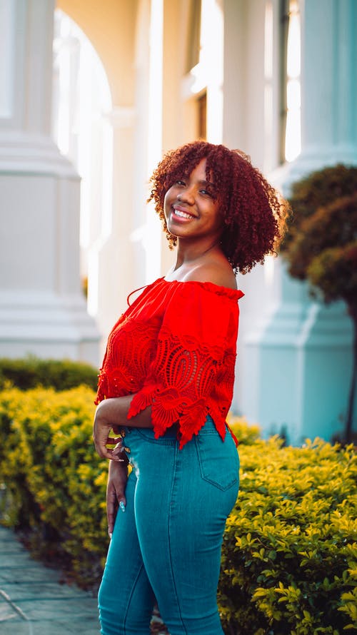 红色掉肩衬衫站在黄色花场附近的女人 · 免费素材图片