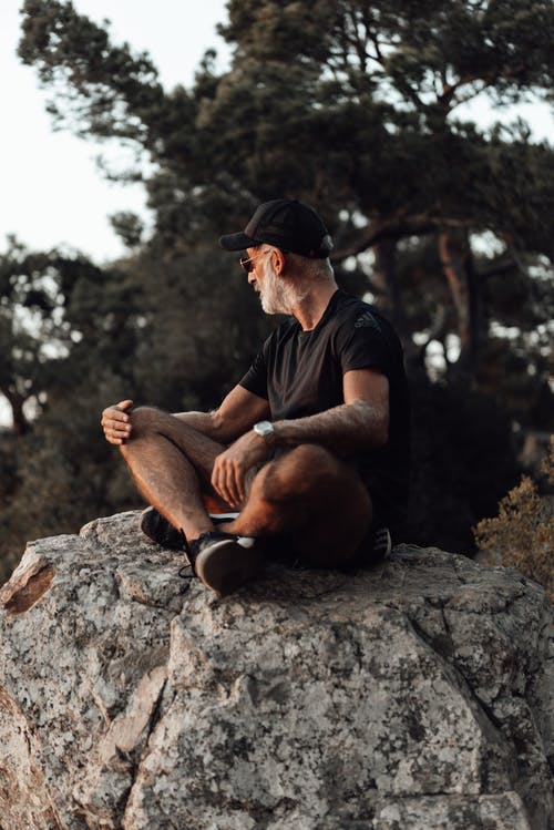黑色的t恤和黑色的帽子，坐在岩石上的人 · 免费素材图片