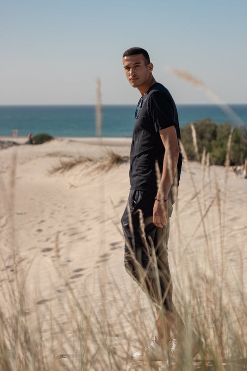 黑色的t恤和棕色的裤子，站在海滩上的人 · 免费素材图片