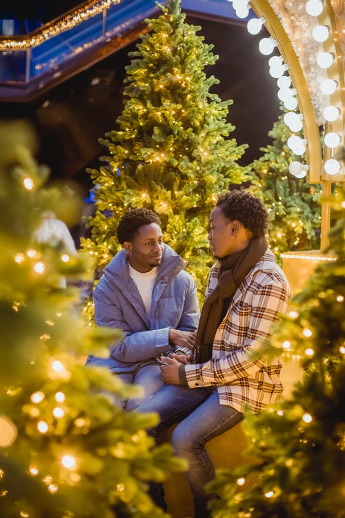 男人和女人坐在圣诞树旁边 · 免费素材图片
