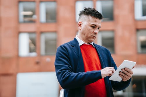 拿着白色片剂计算机的蓝色衣服夹克的人 · 免费素材图片