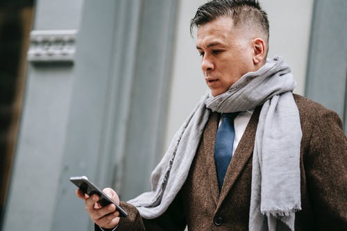 拿着智能手机的棕色外套的男人 · 免费素材图片