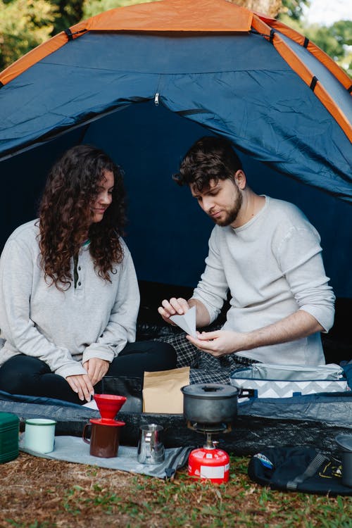 男人和女人坐在蓝色和白色的帐篷上 · 免费素材图片