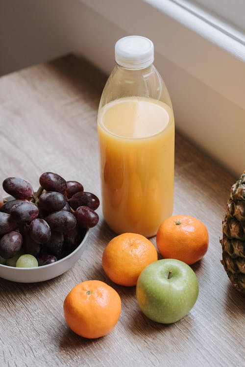 葡萄和葡萄旁边的透明玻璃瓶橙汁 · 免费素材图片