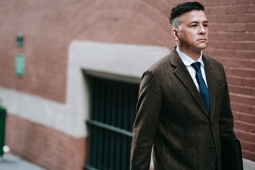 黑色西装站在棕色墙附近的男人 · 免费素材图片