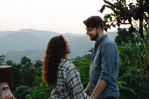 男人和女人坐在棕色的木凳上，看着绿山 · 免费素材图片