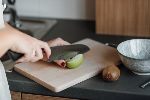 在褐色的木砧板上切绿色蔬菜的人 · 免费素材图片