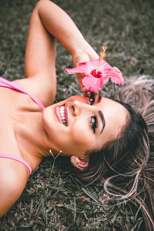 躺在粉红色的花，她的耳朵上的棕色草地上的粉红色背心的女人 · 免费素材图片
