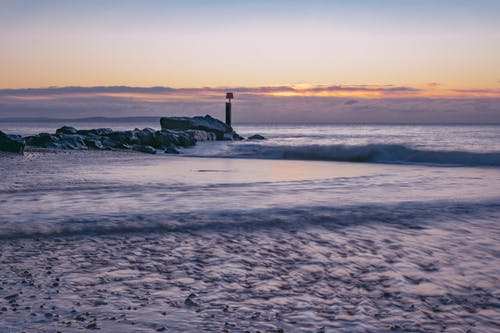海浪在日落期间在海岸上崩溃 · 免费素材图片