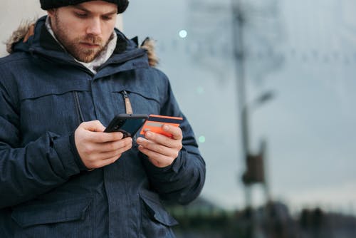 拿着黑色智能手机的黑色外套的男人 · 免费素材图片