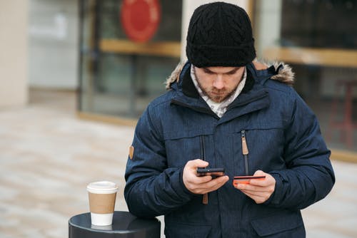 黑色针织帽和黑色外套拿着智能手机的人 · 免费素材图片
