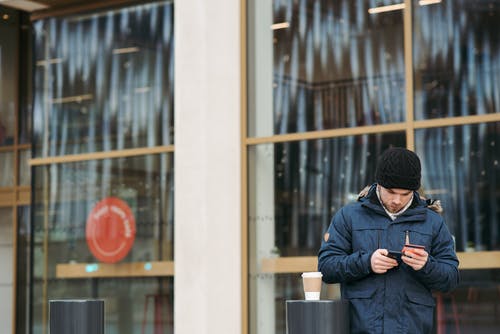 黑色针织帽和蓝色外套拿着白色陶瓷杯的男人 · 免费素材图片