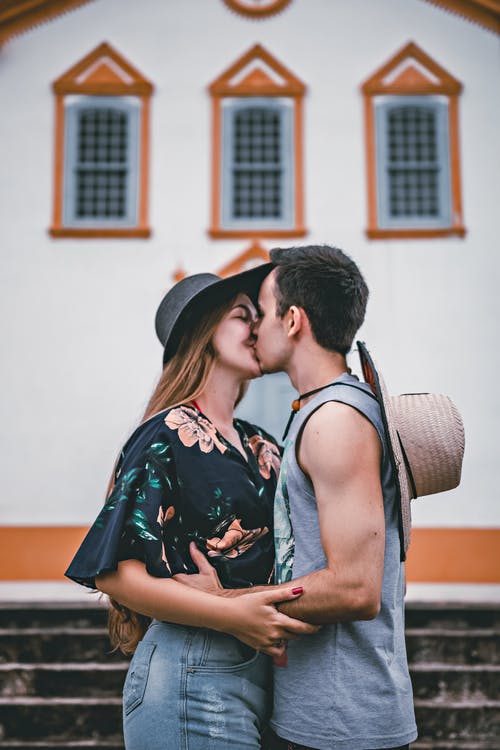 男人和女人在白墙附近接吻 · 免费素材图片