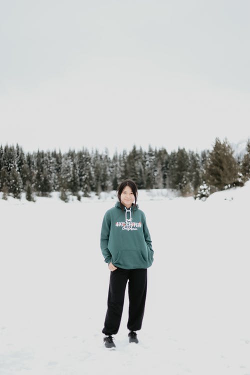 绿色毛衣和黑色的裤子，站在积雪的地面上的女人 · 免费素材图片