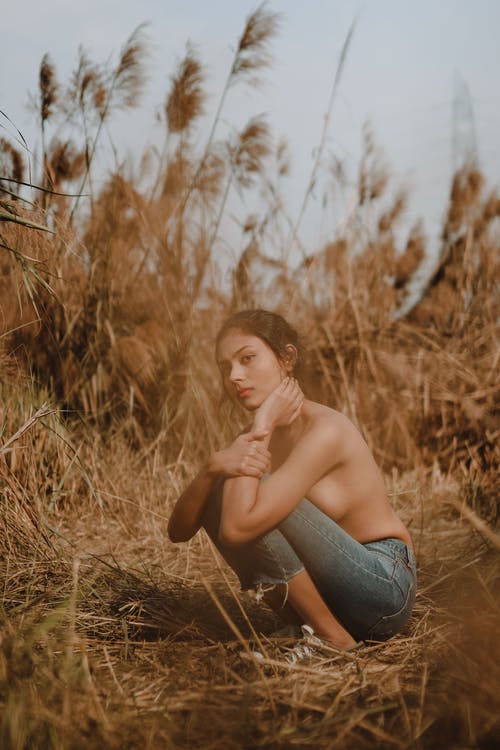 裸照女人坐在棕色的草田 · 免费素材图片
