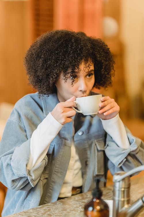拿着白色陶瓷杯子的蓝色牛仔夹克的女人 · 免费素材图片